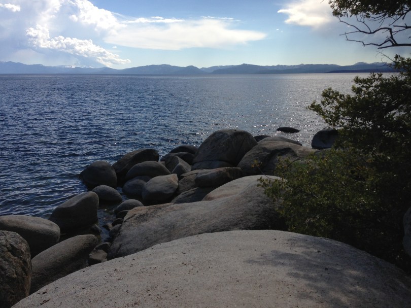 Lake Tahoe with rocks in foreground and blue sky with clouds above
